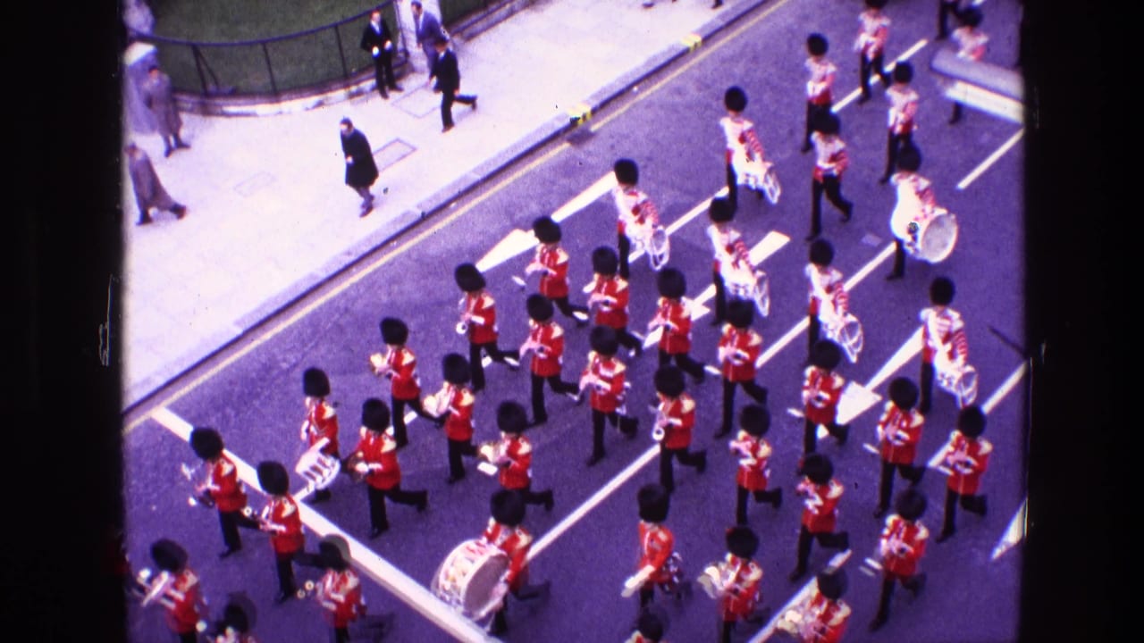 Marching band members in red uniforms advance in rows with brass instruments and drums.