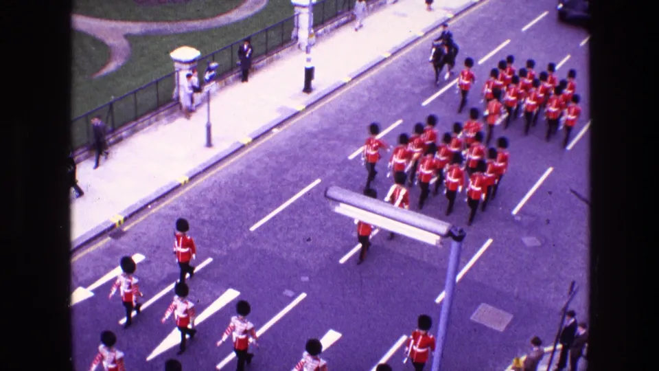 Elevated 1969 home-movie view of a compact military band formation in red uniforms moving through an urban roadway.