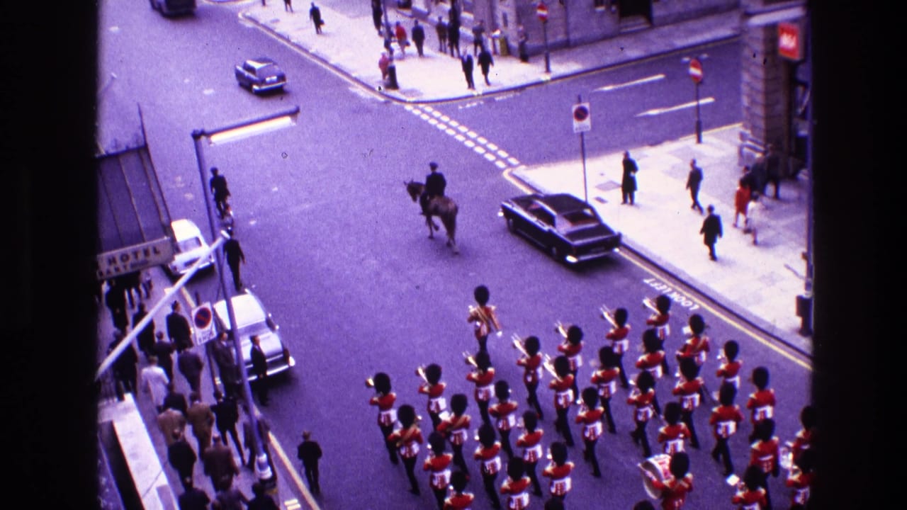 Mounted figure and marching guards move through an intersection with pedestrians on the sidewalks.