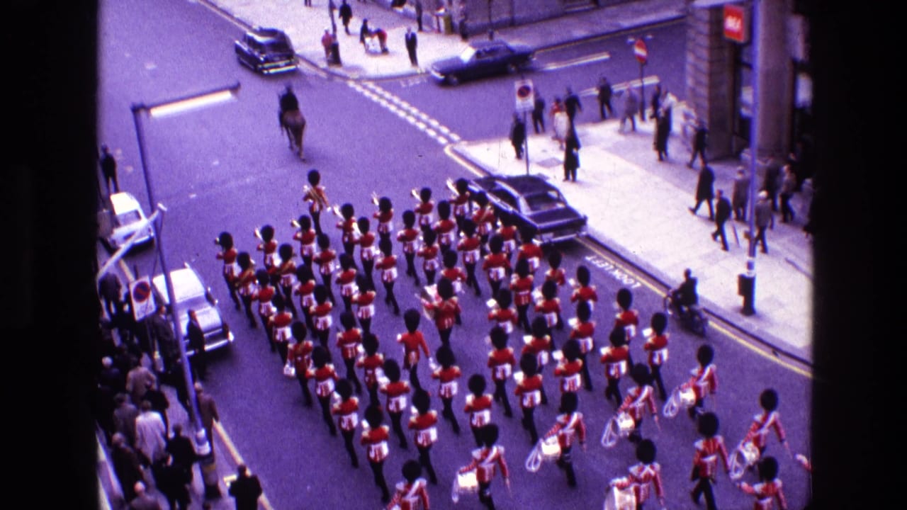 Rows of uniformed musicians march along the street with cars and pedestrians around the route.