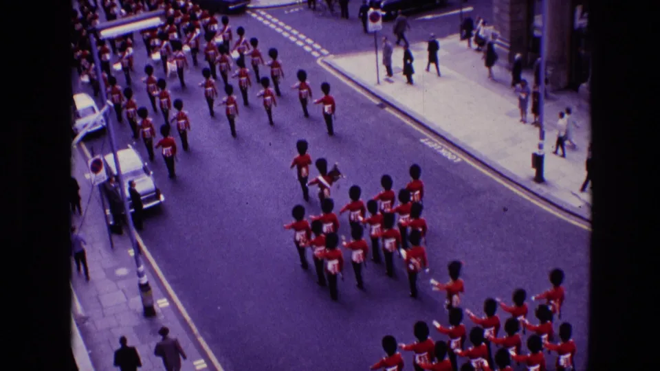 High-angle 1969 Ireland parade footage showing red-uniformed marchers, black hats, city sidewalks, and spectators along the route.
