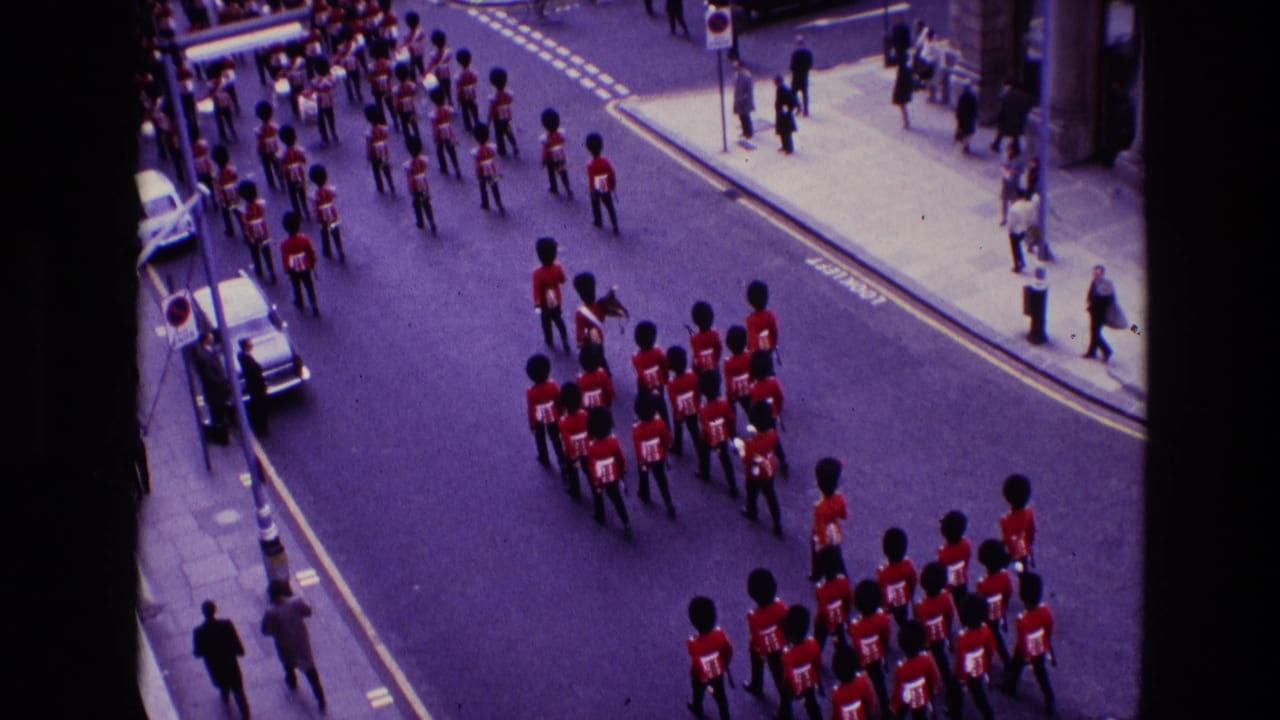 Guards in red tunics march down a city street as spectators watch from the pavements.