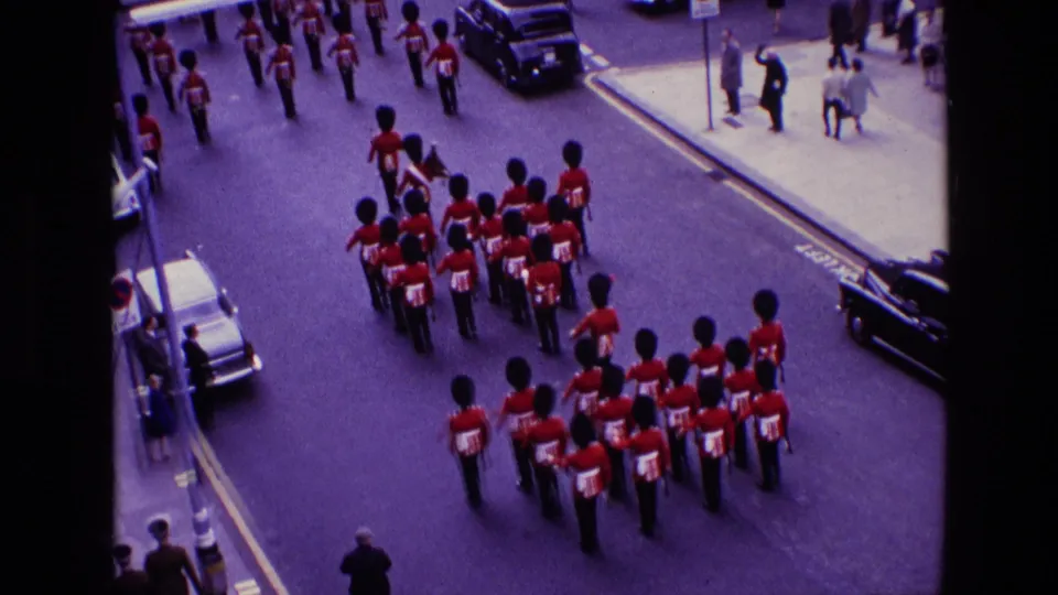 1969 8mm view of Queen's Guards marching away along a London street, with spectators and vehicles at the edges.