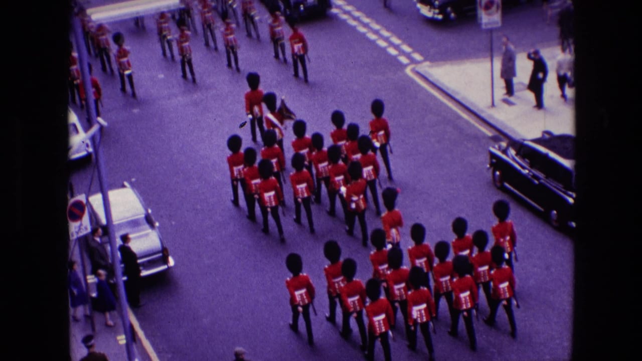 1969 Ireland home-movie frame showing royal guard members in red tunics and bearskin hats marching below an elevated camera.
