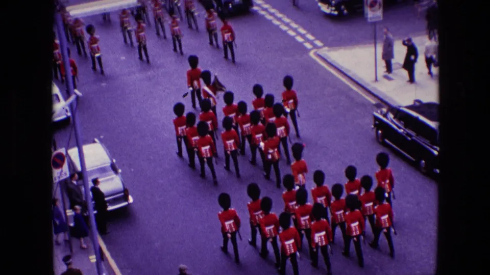 1969 Ireland home-movie frame showing royal guard members in red tunics and bearskin hats marching below an elevated camera.
