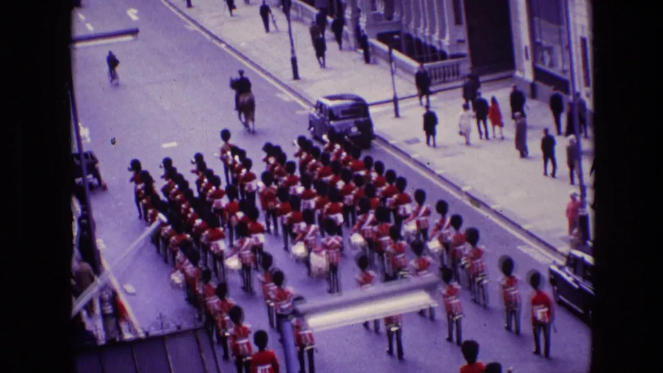 1969 Ireland street scene with a guard band, drums, red uniforms, spectators, vehicles, and a mounted officer visible from above.