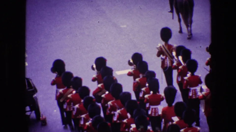 Elevated 8mm view of uniformed band members in red ceremonial dress marching in formation during an Ireland parade.