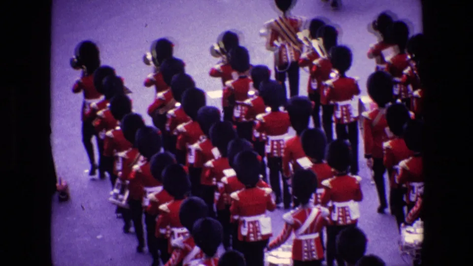 1969 Ireland parade frame with red-uniformed military musicians and tall black hats passing below the camera.