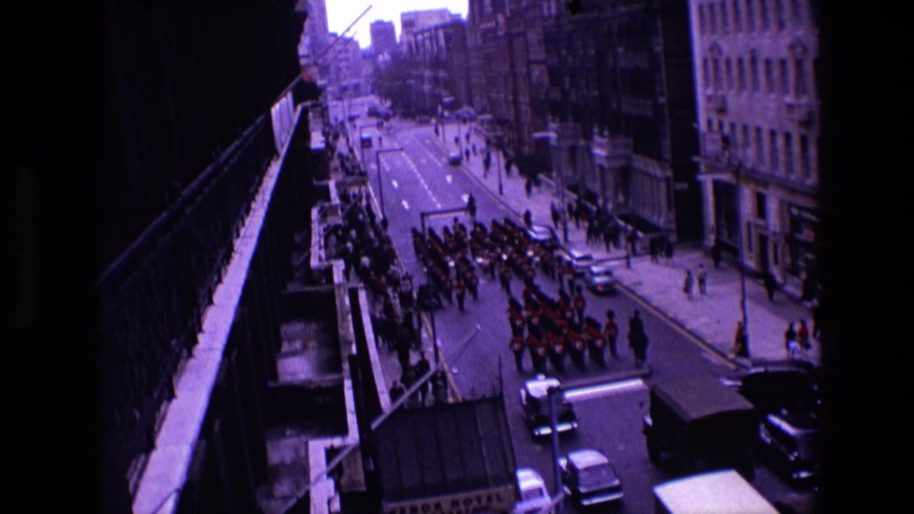 Marching band passes along a wide city street with cars and pedestrians nearby.