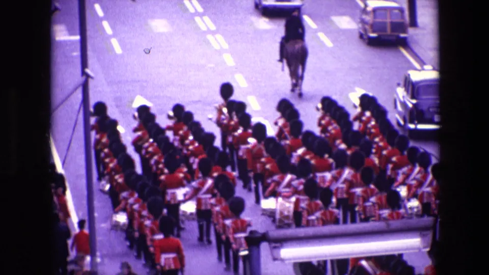 Closer balcony view of the red-uniformed marching band, with drums and brass visible and a mounted rider ahead on the road.