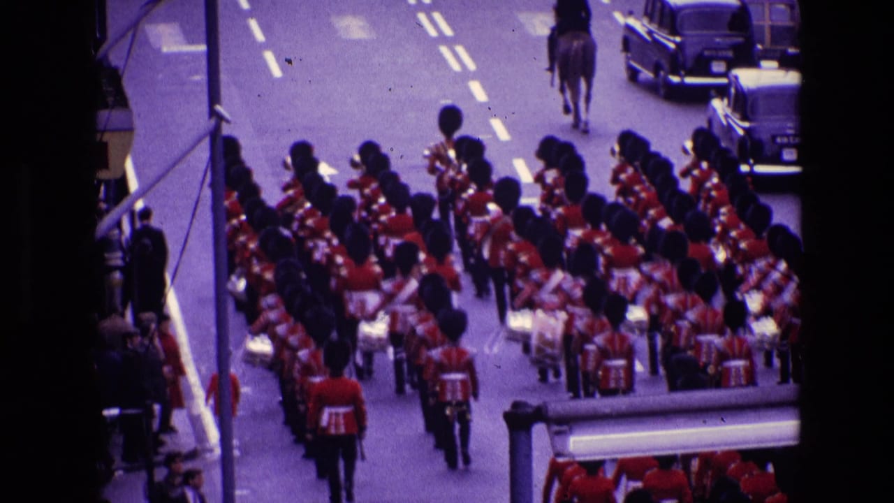 1969 Ireland 8mm frame showing a marching band in red uniforms and tall black hats moving down a city street.