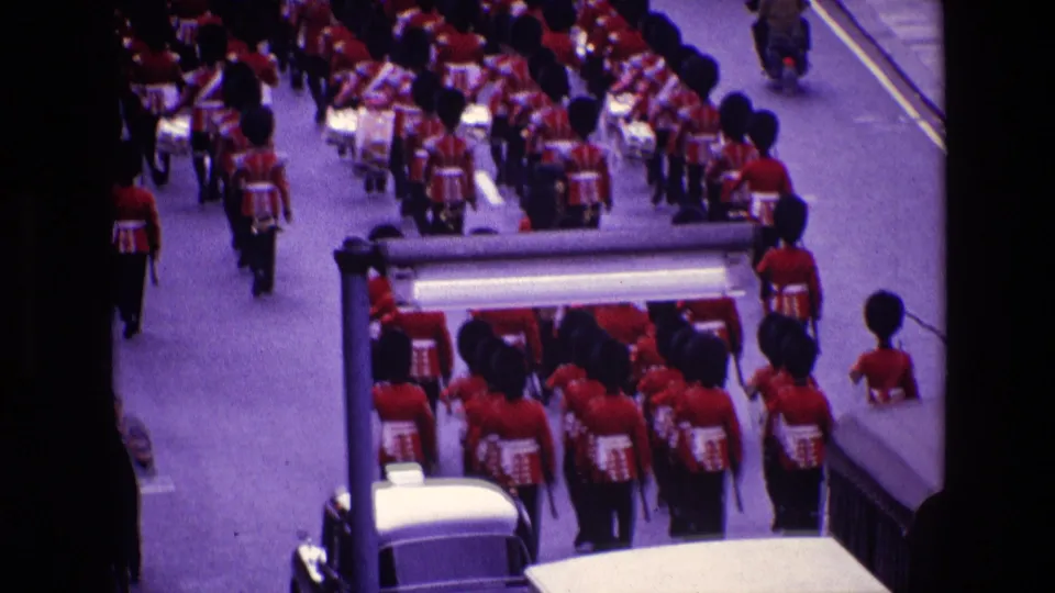1969 Ireland parade view with red-uniformed musicians, tall black hats, a mounted officer, and 1960s vehicles.