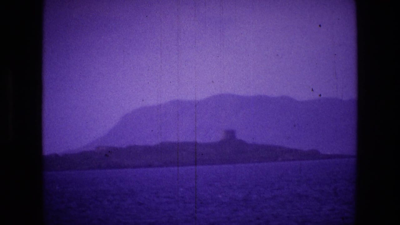 Purple-tinted sea view with a distant island or headland and small tower on the shoreline.