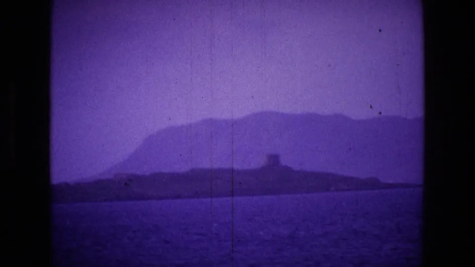 Purple-tinted 8mm coastal view in Ireland, with open water, a distant island or headland, and a small tower-like structure.