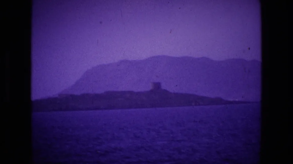 Ireland coastal landscape from 1969 home-movie footage, showing dark water, a distant island or headland, and a small shoreline tower.