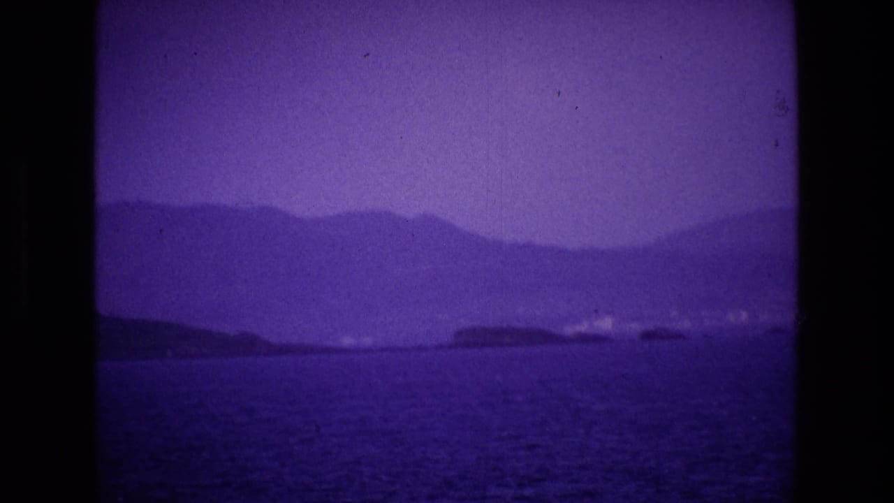 Distant coastal hills and small landforms across a purple-tinted sea.