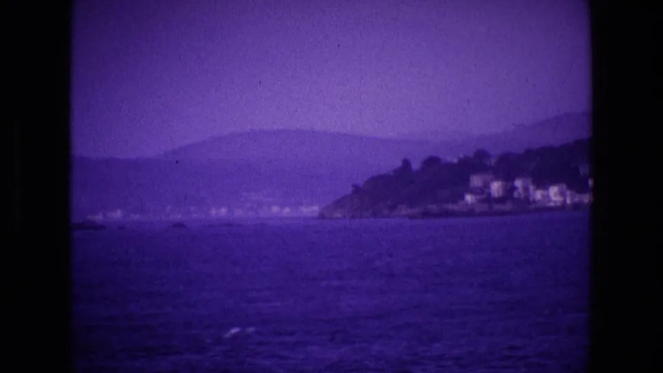 Ireland, 1969: offshore view of a small coastal settlement on a wooded headland beneath hazy mountains.