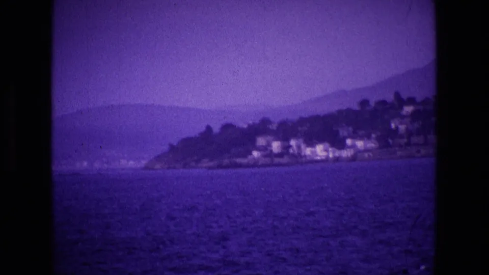 Purple 8mm frame showing an Irish coastal hillside with white buildings, dark trees, water, and misty mountains beyond.
