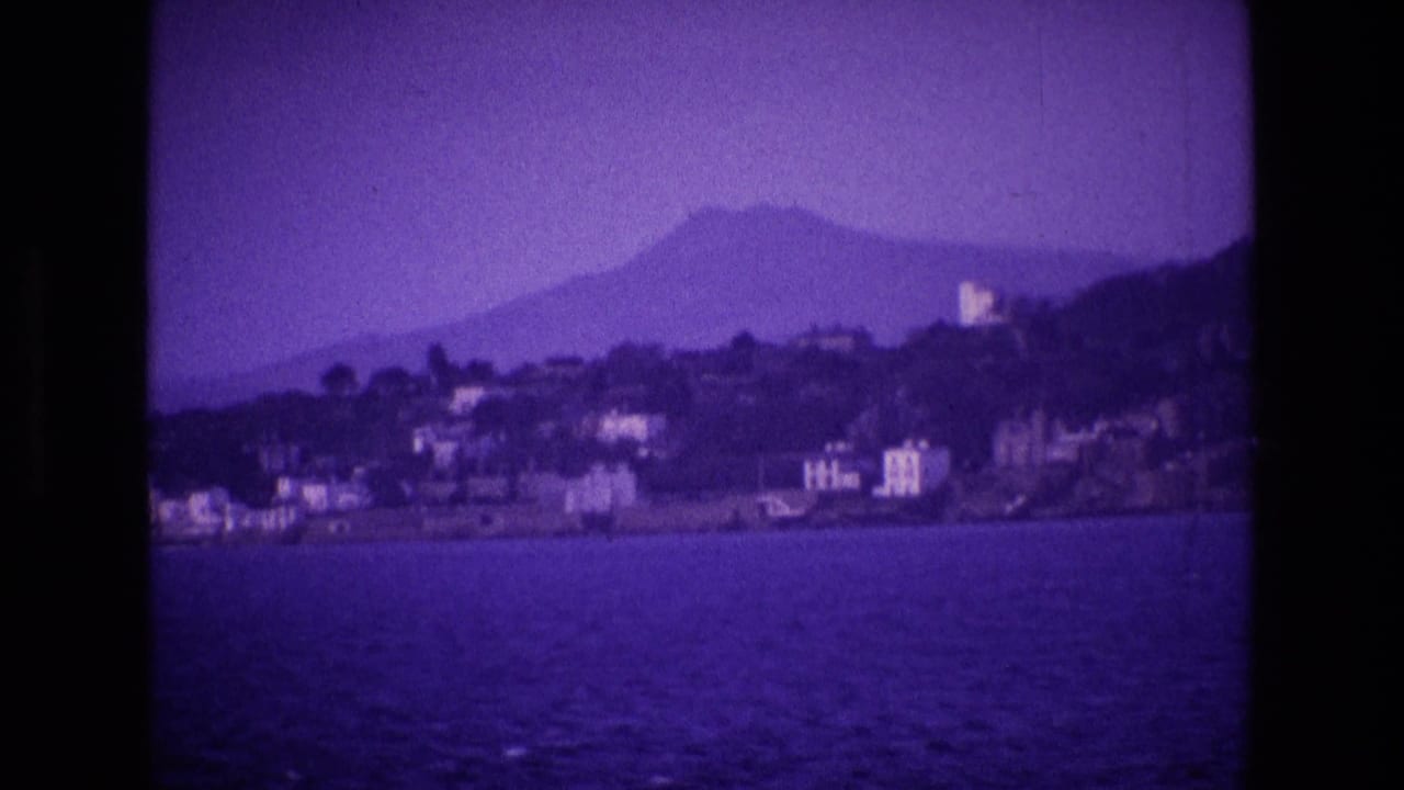 Distant coast across water with clustered buildings, a hillside, and a mountain silhouette.