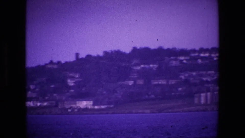 1969 Ireland 8mm view of houses scattered on a hillside above the sea, seen from across the water with a purple film tint.