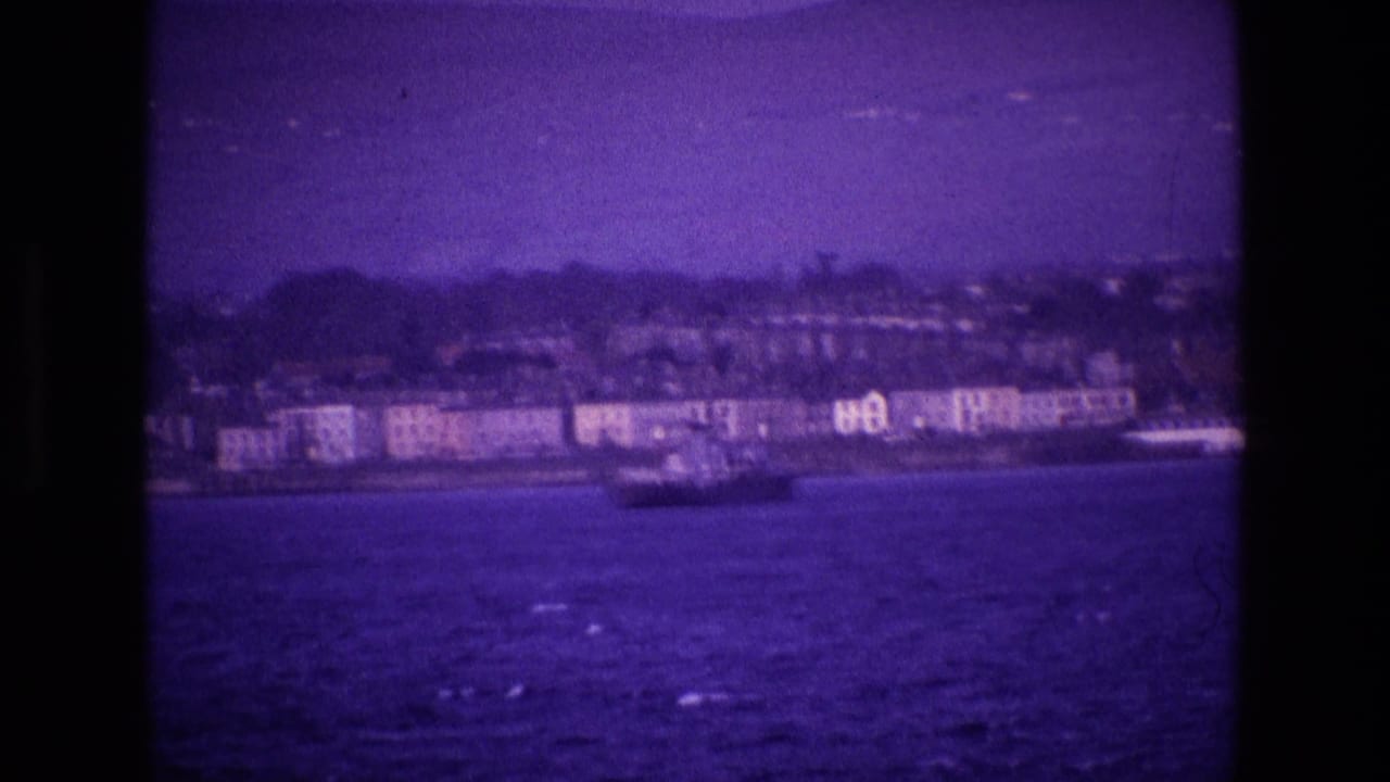 Coastal buildings and a vessel across dark water under a purple-tinted sky.