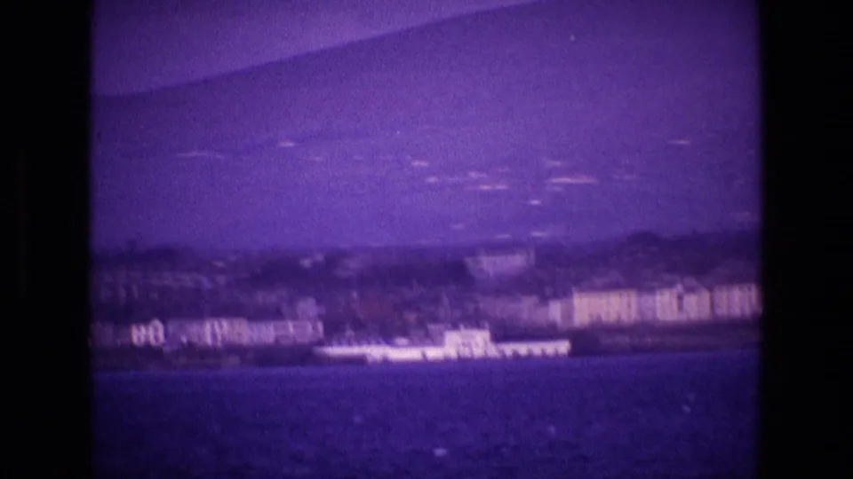 Soft 8mm frame of an Irish coastal town from the water, with shoreline buildings and a white vessel visible through purple color shift.