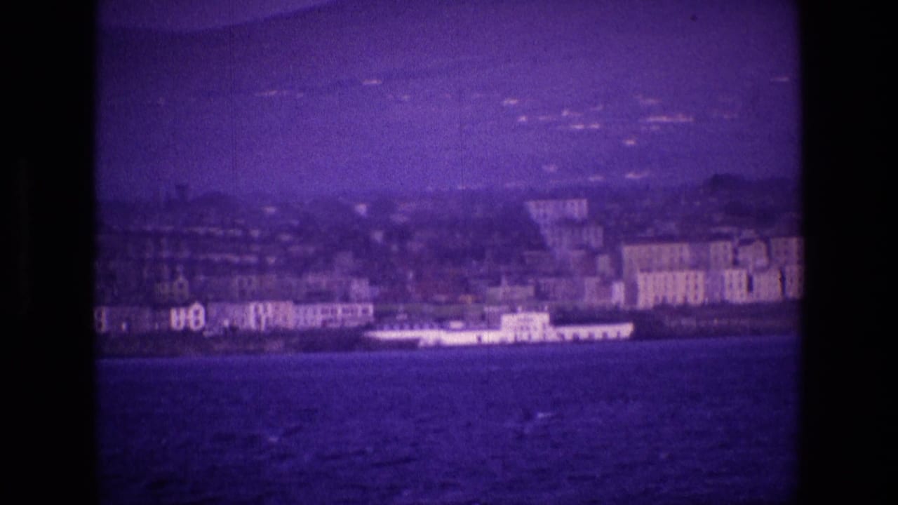 Purple-tinted coastal town seen across open water with buildings along the shore.