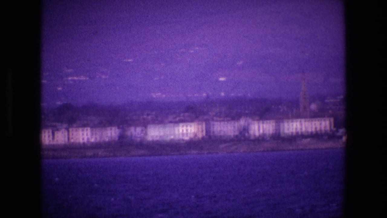 Distant waterfront town across dark water under a purple-tinted sky.