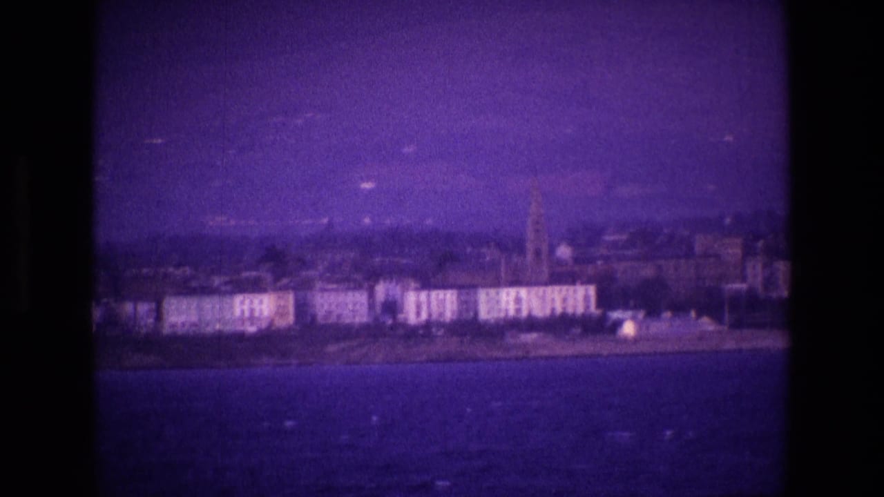 A soft 8mm view of an Irish coastal town, with waterfront buildings and a tall church spire under a purple cast.