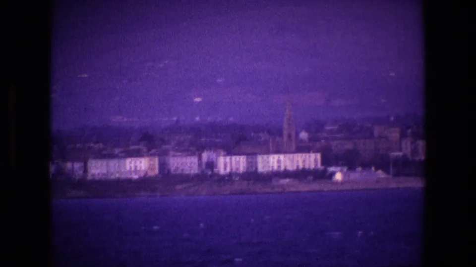 A soft 8mm view of an Irish coastal town, with waterfront buildings and a tall church spire under a purple cast.