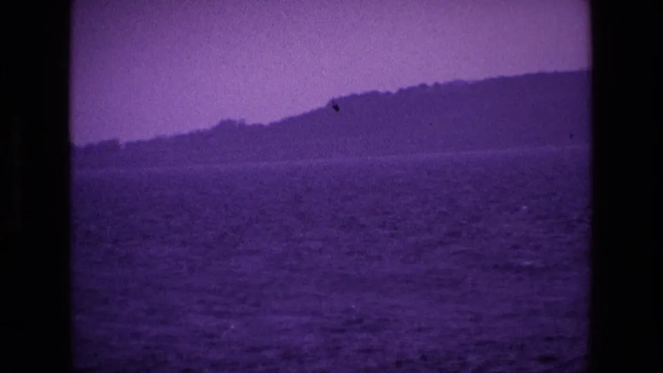 1969 8mm Ireland seascape with sloping coastal hills, open water and visible film wear in the frame.