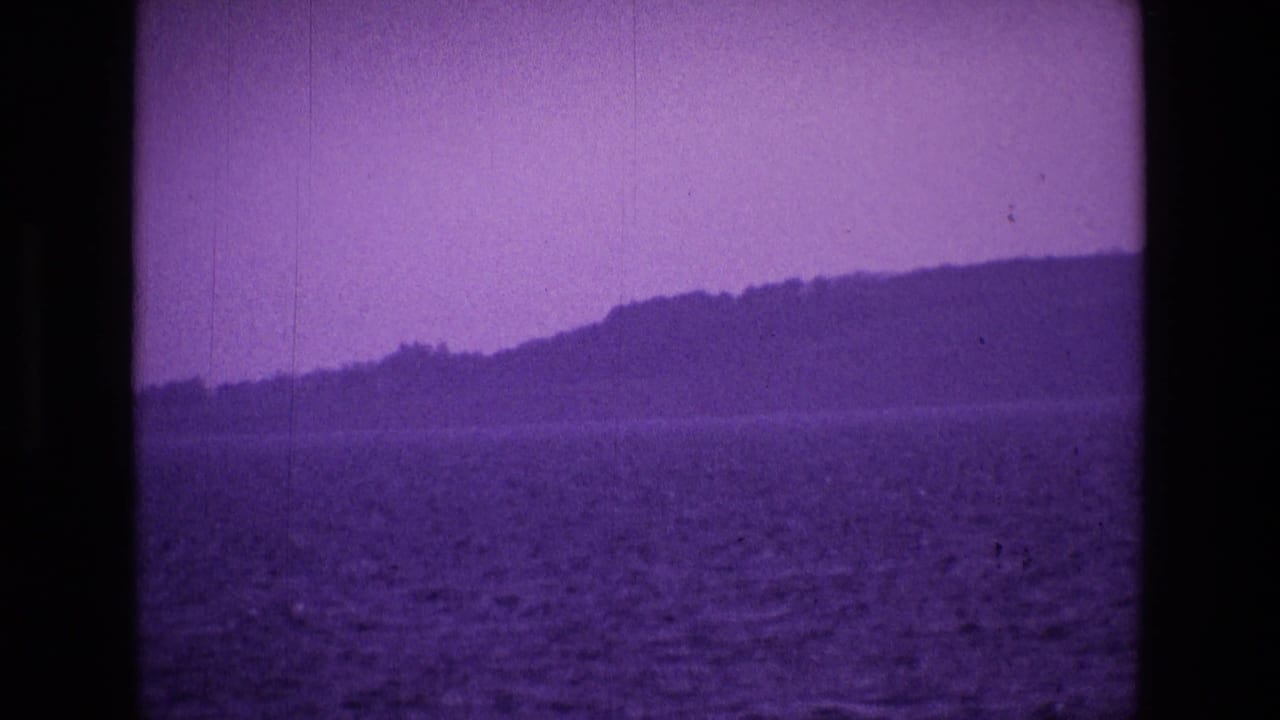 1969 Ireland 8mm frame showing rippled water from a boat, a distant shoreline, and low hills under a purple color cast.