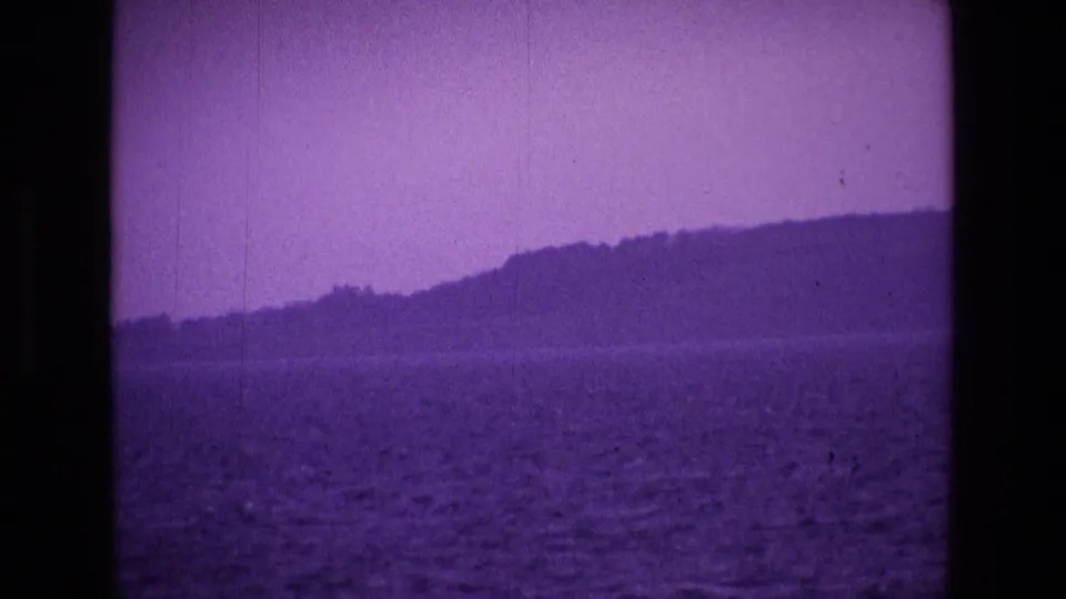 1969 Ireland 8mm frame showing rippled water from a boat, a distant shoreline, and low hills under a purple color cast.