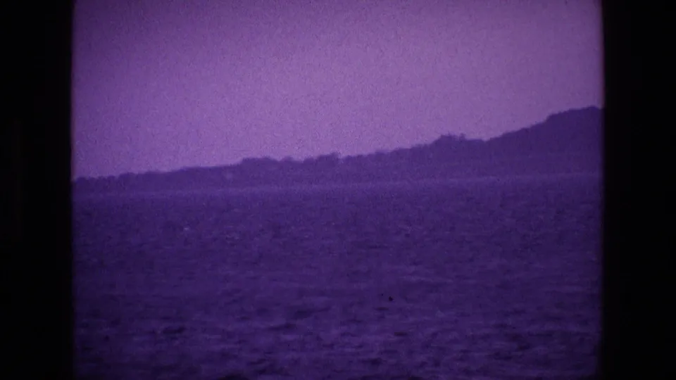 1969 Ireland 8mm frame with a hilly coast or lakeshore across rippled water, seen through dark frame edges.