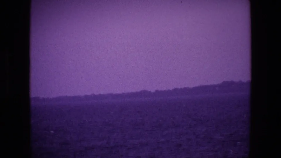 1969 Ireland 8mm frame showing a low distant shore across dark water, with a soft purple sky and visible film texture.