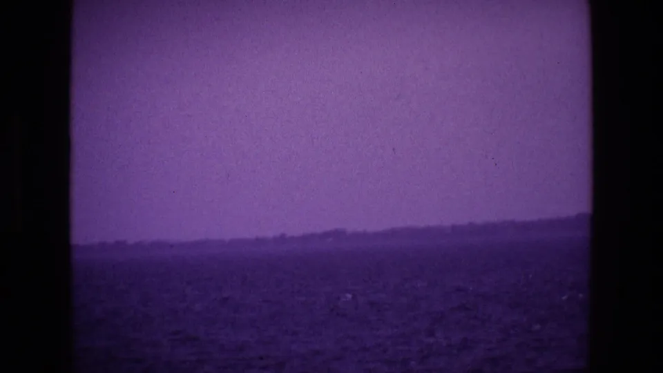 1969 Ireland 8mm frame of water and a low coast or lakeshore receding beneath a purple haze.