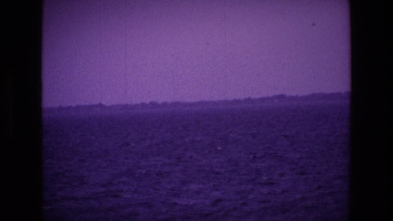 Purple-tinted open water with a hazy distant shoreline and dark film borders.