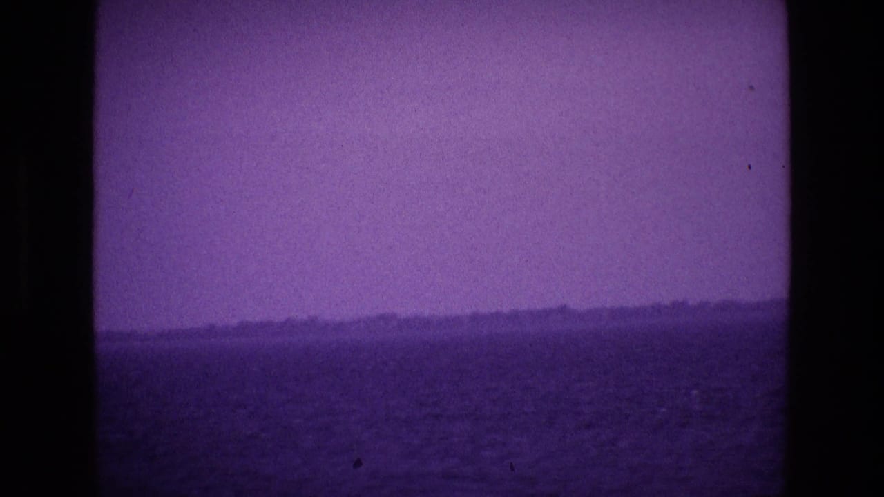 Hazy water and low shoreline framed by dark vertical film or boat edges.