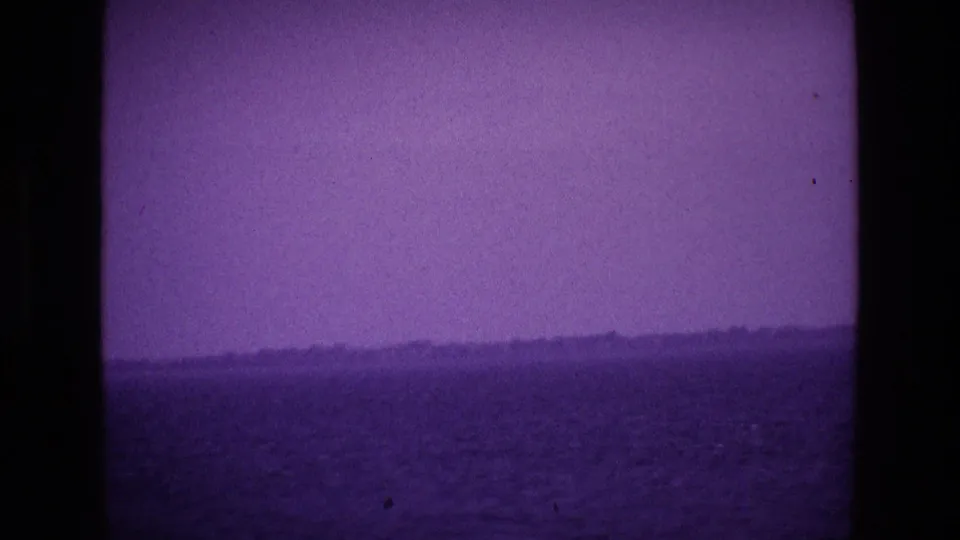 Purple-shifted 8mm view across water toward a low Irish shoreline, framed by dark vertical edges.