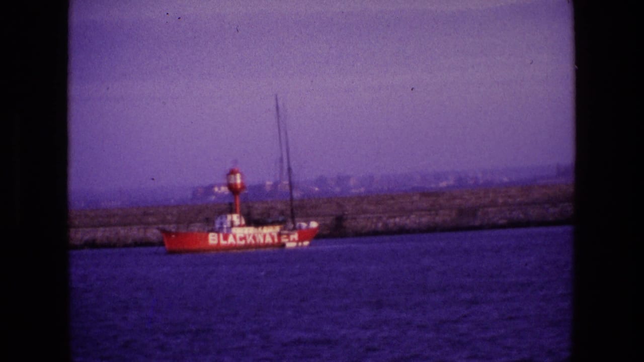 1969 Ireland 8mm frame with the red BLACKWATER vessel passing in front of a stone harbor wall under a hazy sky.