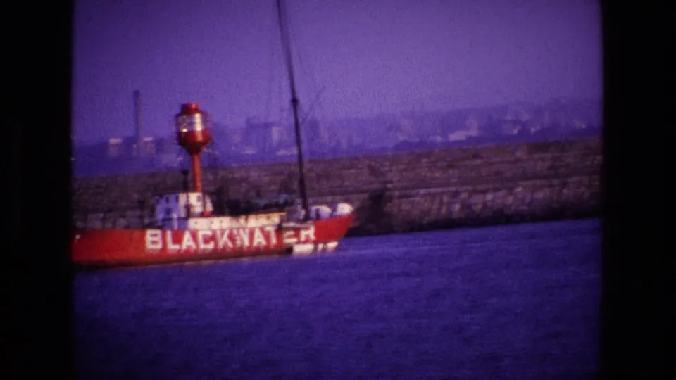 1969 Ireland 8mm frame with the red BLACKWATER vessel near the lower frame, backed by harbor water, wall, and distant structures.