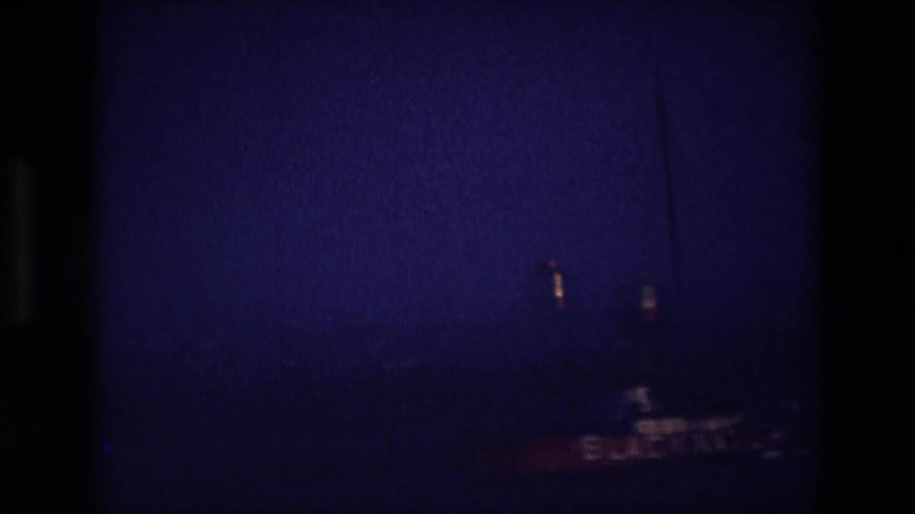 Dark underexposed frame with a faint boat shape and film border.