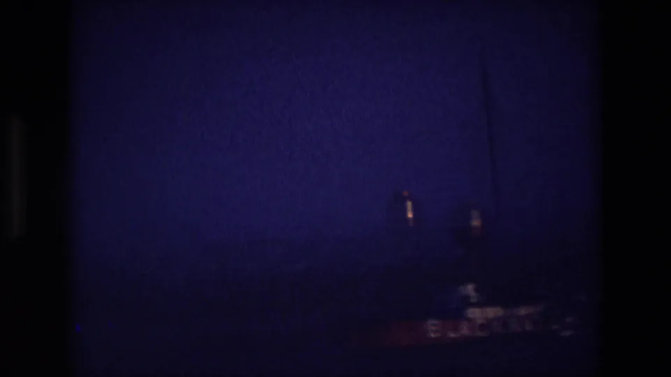 Underexposed 8mm frame from the Ireland reel with a barely visible vessel shape behind dark gate shadows.