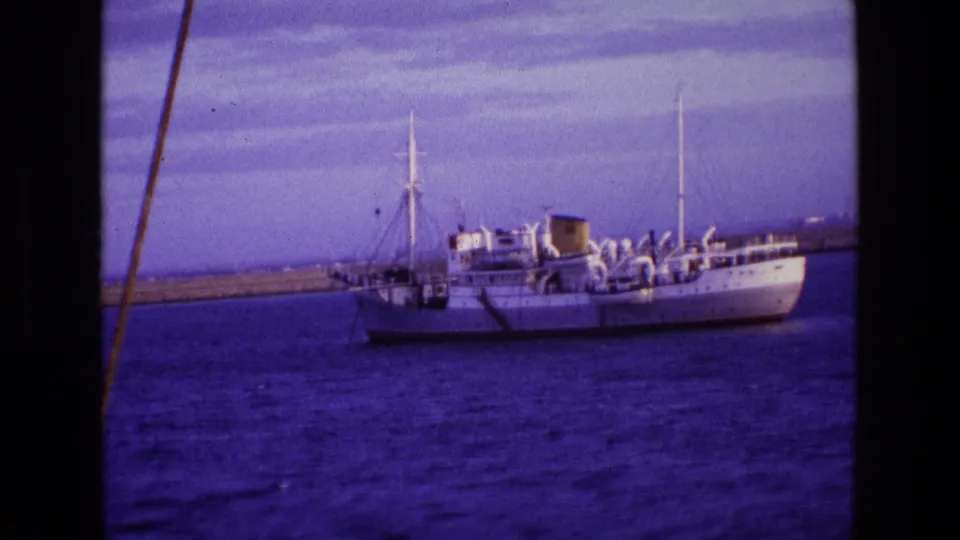 White passenger vessel on open water in Ireland, with masts, deck structures, and a low harbor wall in the distance.