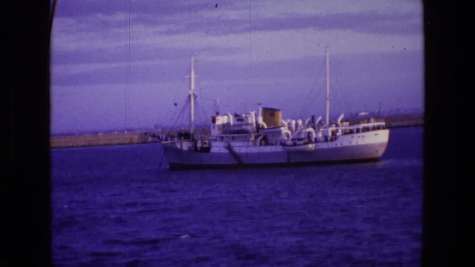 1969 Ireland home-movie frame showing a white passenger boat centered on open water with masts and deck fittings.