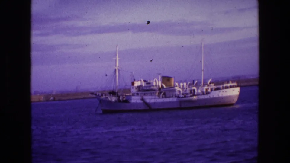 A softer 8mm frame shows the white ship anchored off Ireland in 1969, with deck structures and a low breakwater in view.