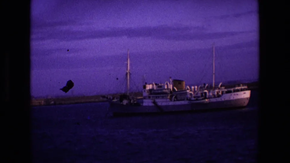 Near dusk, the 1969 Irish footage renders the anchored ship darker against blue water and a purple sky.