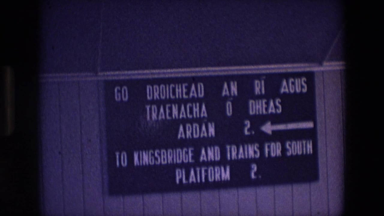 1969 Ireland 8mm frame showing a bilingual station sign directing passengers to Kingsbridge and southbound trains on Platform 2.