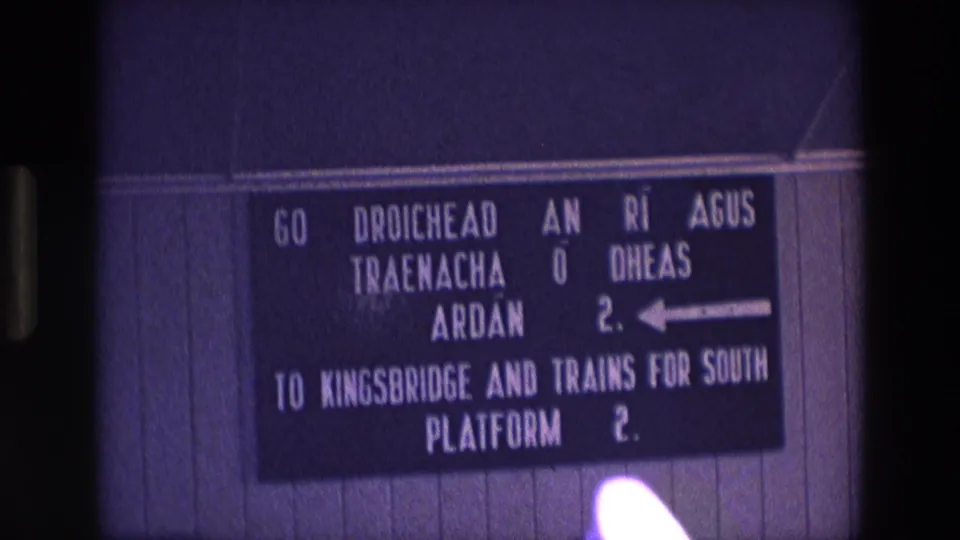 Final 8mm frame of the Irish station sign, with bilingual direction text and a bright light leak at the bottom of the scan.