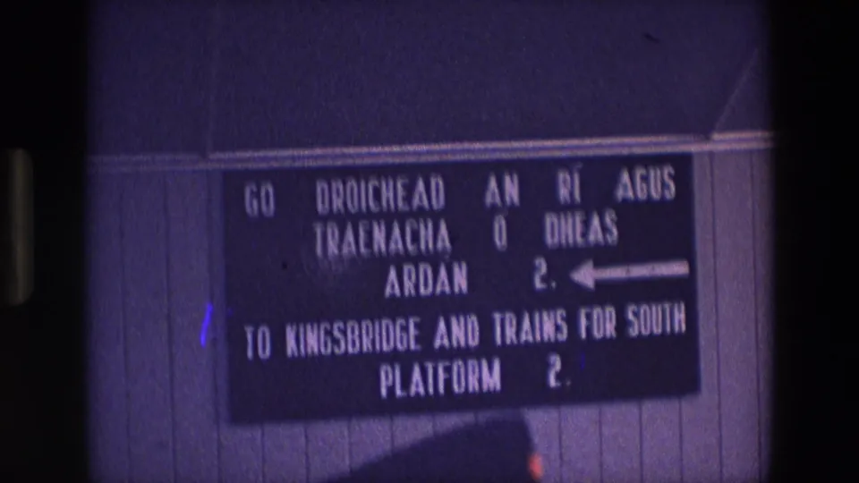 1969 Ireland 8mm frame showing a bilingual station sign directing passengers to Kingsbridge and southbound trains via Platform 2.